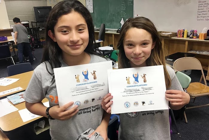 Two girls holding C.A.R.E.4Paws Paws Up Youth Program Certificates