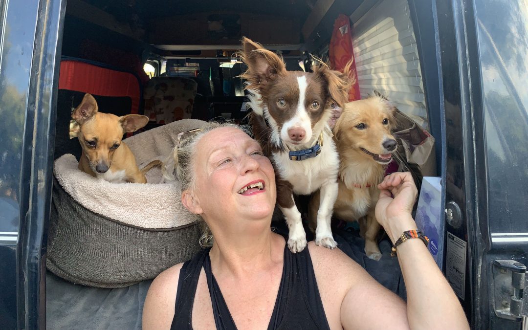 An unsheltered pet owner sitting near the back of her van with her pets